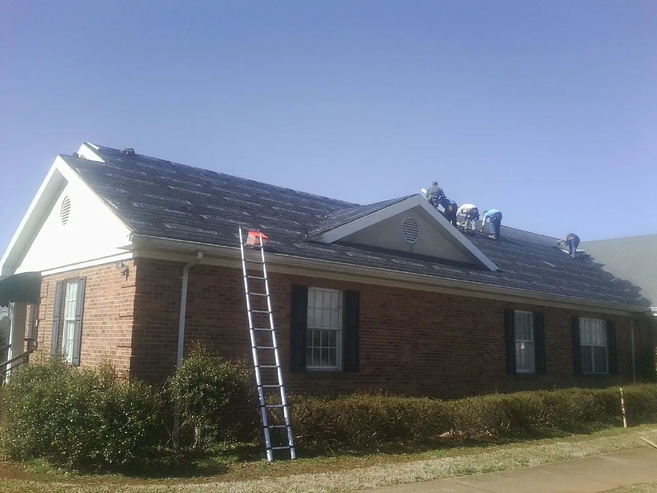 Crew tearing shingles off a brick ranch roof with a ladder set — Emergency Roof Repair work by our crew in Gower