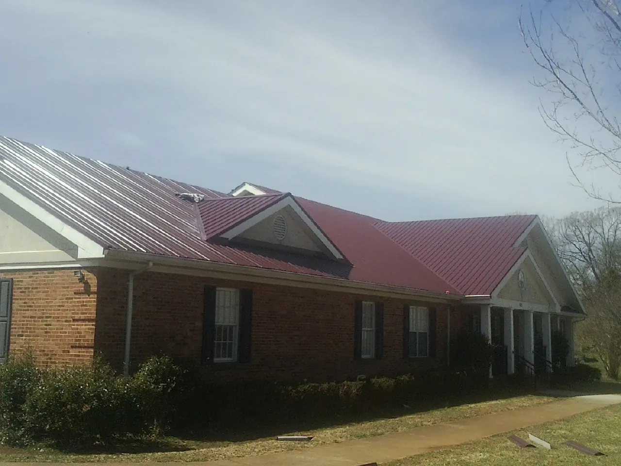 Red metal roof with gabled entries on a long brick building, from a Hail Damage Roof Repair job in Gower