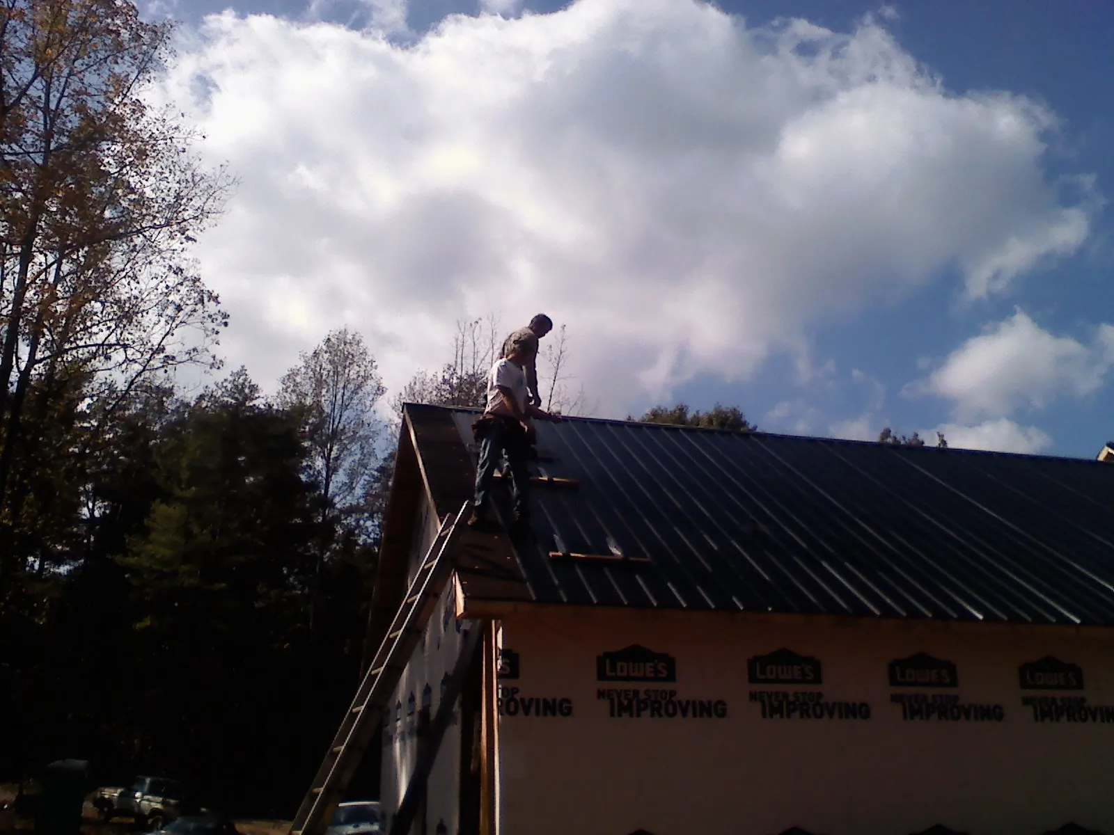 Roofer fastening dark metal panels high against a cloudy sky, from a Roof Inspection job in Gower